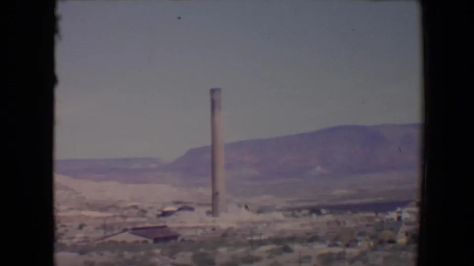 End frame from a 1967 Flagstaff, Arizona 8mm shot showing a smokestack, scattered buildings, scrubland, and mountain backdrop.