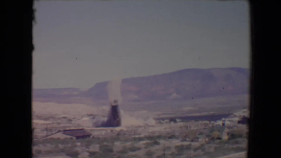 1967 Flagstaff 8mm frame showing the tower breaking down with a plume of dust rising near low industrial structures.