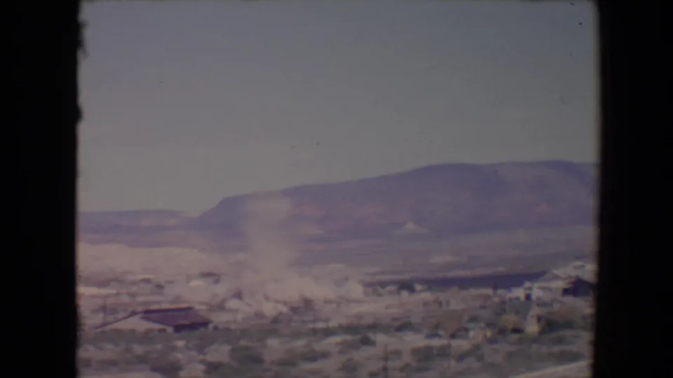 1967 Flagstaff-area demolition frame with the tower mostly down and a widening dust cloud across the desert industrial site.