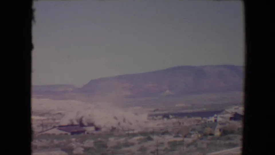 The 8mm frame shows a widening demolition dust cloud moving across low structures in Flagstaff, Arizona, with mountains beyond.