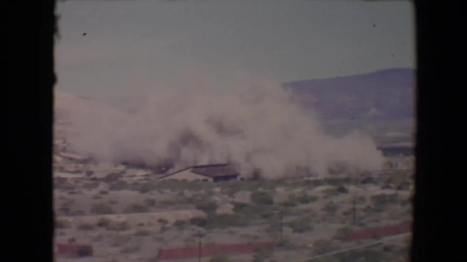 A widening smoke or dust cloud covers part of a low desert building in the 1967 Flagstaff, Arizona home-movie footage.