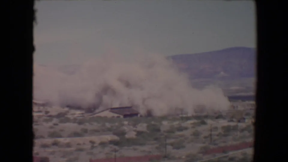 Thick smoke or dust spreads laterally over desert scrub and a low structure in the 1967 Flagstaff, Arizona clip.