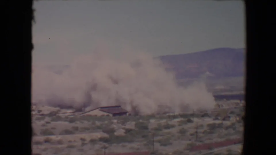 1967 Flagstaff, Arizona home-movie frame of a dense smoke cloud spreading near a low building in open desert terrain.