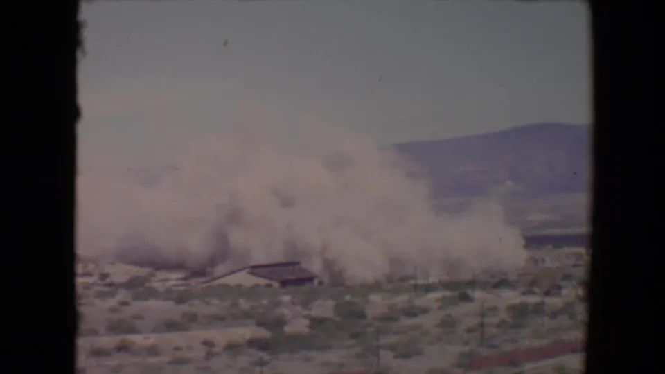 Faded 8mm frame from 1967 showing a smoke cloud thickening over scrubland near a low building in the Flagstaff, Arizona area.