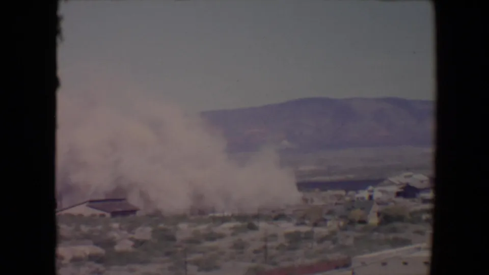 1967 Flagstaff, Arizona view of a thick smoke cloud moving over low structures in a dry landscape.