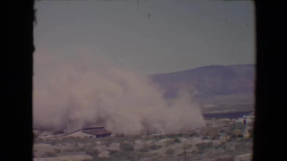 1967 Flagstaff, Arizona 8mm frame showing dense smoke over a sparse desert settlement below hills.