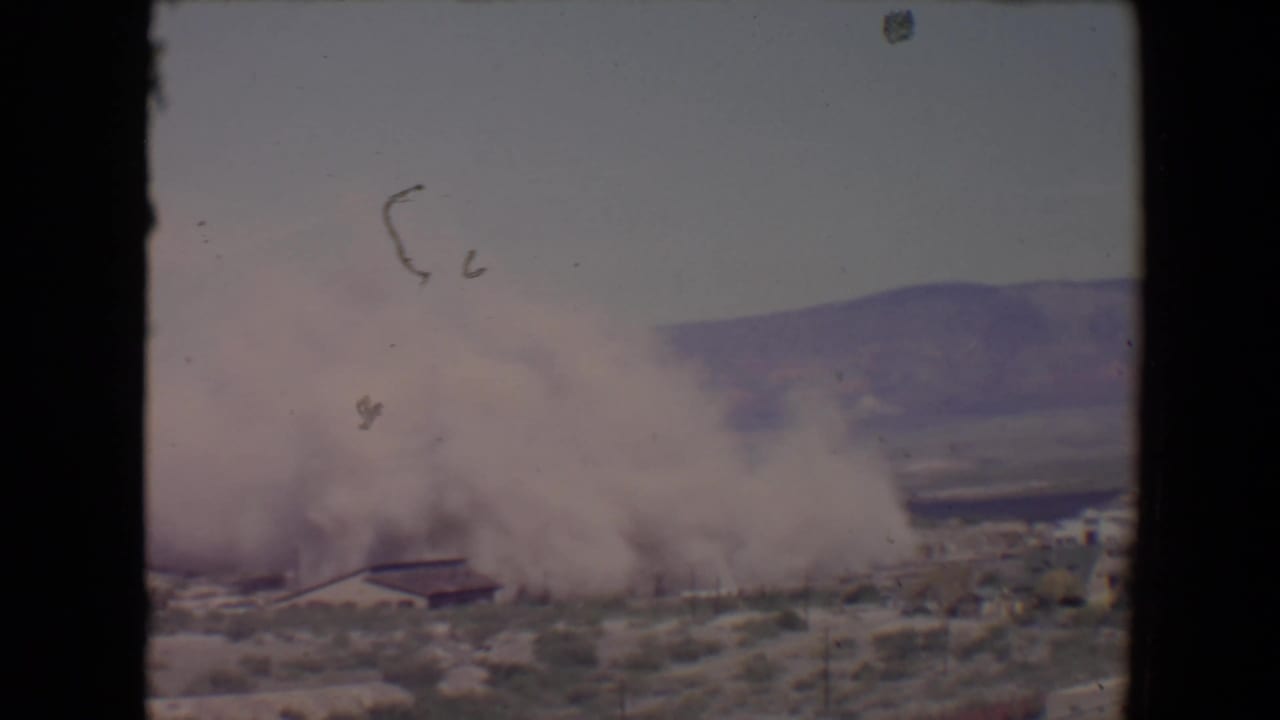 Dust cloud rising near a low building in a desert landscape.