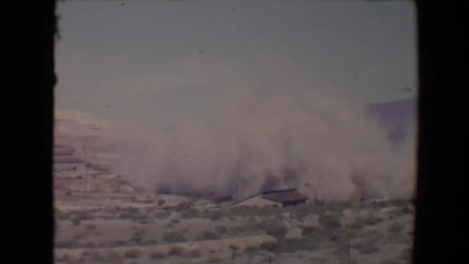 1967 Flagstaff-area frame with a broad dust cloud moving over scrubland and partly obscuring a low structure.