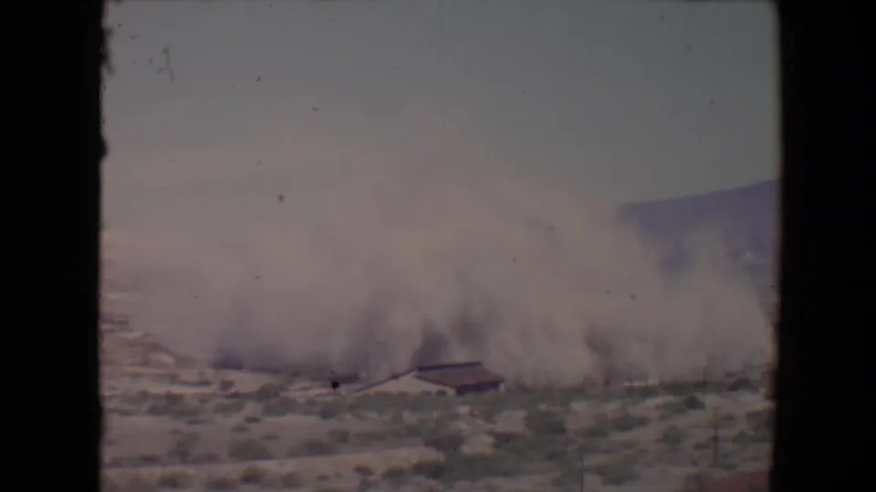 1967 Flagstaff-area 8mm frame showing dense dust and debris cloud covering much of a low desert structure.