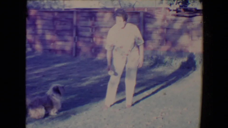 The woman stands on a sunlit gravel area with a small dog nearby, likely during a fetch game in Tucson, Arizona.