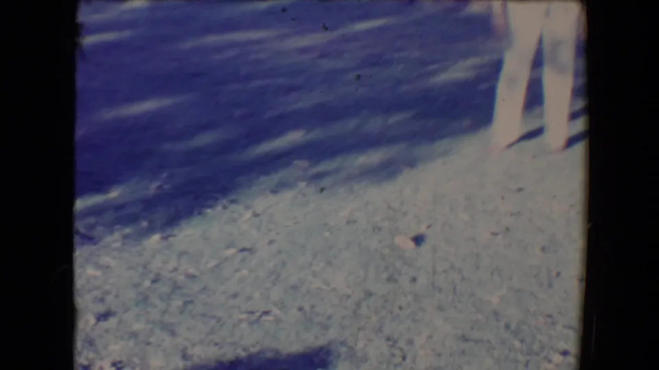 A partial 8mm frame shows the woman's legs on a bright gravel path, with the dog mostly outside the visible area.