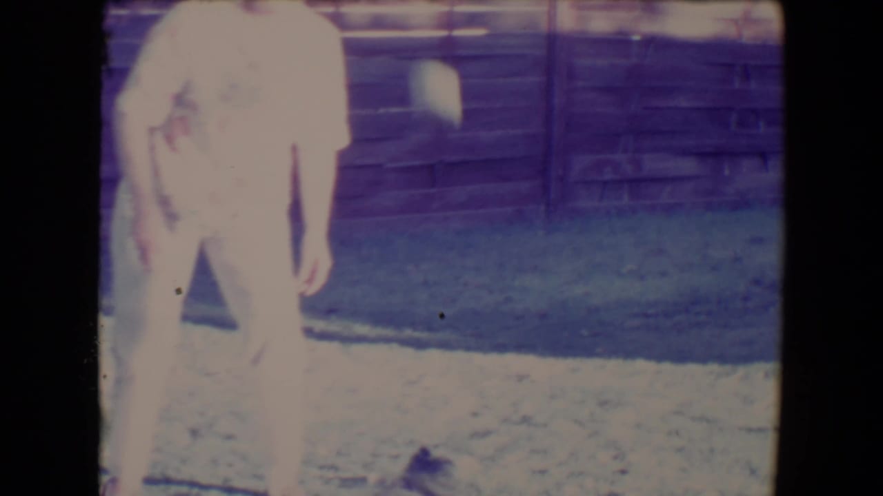 Woman in light clothing standing on grass near a wooden fence.