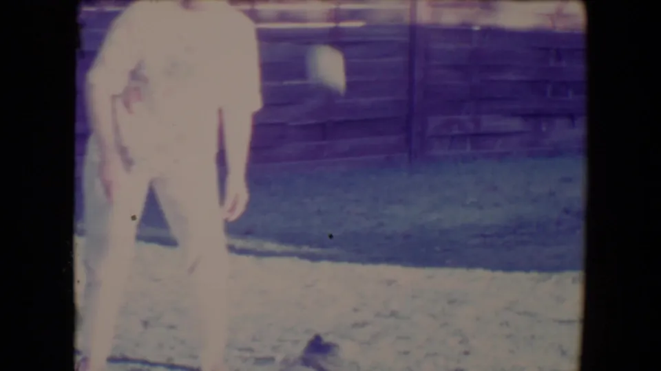 A soft, overexposed 8mm frame shows the woman standing in the Tucson backyard near the wooden fence.