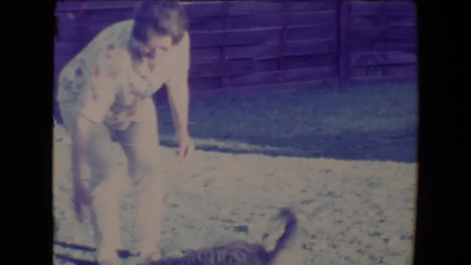 The woman bends toward a small dog in the fenced Tucson yard, likely during a fetch moment captured on 8mm film.