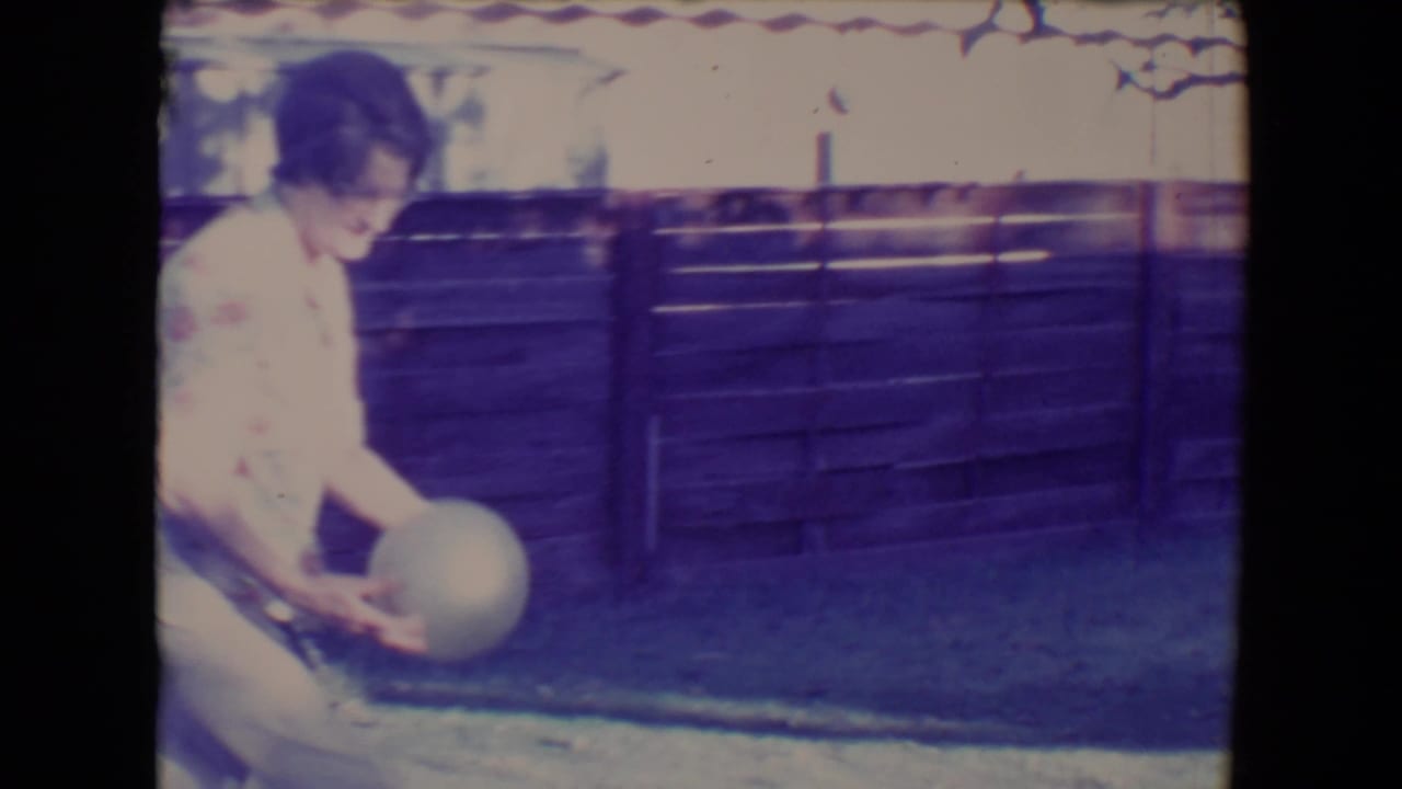 Woman holds a pale ball while standing on grass in front of a wooden fence.