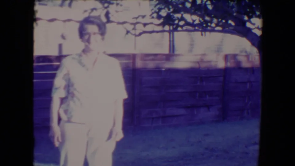 The woman stands facing the camera in the 1967 Tucson yard, with tree branches above and a wooden fence behind her.