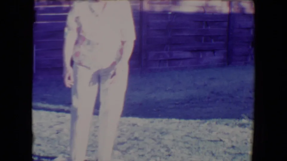 A woman in a patterned shirt and light pants stands in the bright Tucson backyard, framed by grass and a wooden fence.