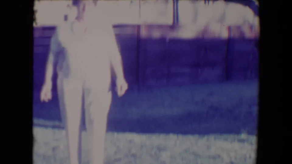 A soft, overexposed home-movie frame shows the woman partly cropped as the small dog moves beside her in the backyard.