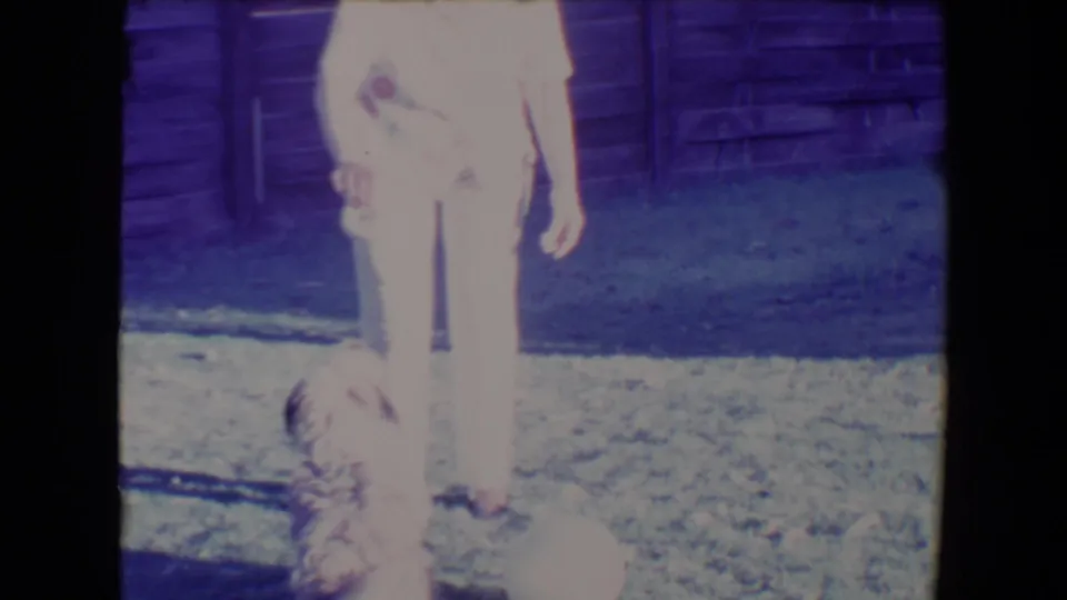 1967 Tucson home-movie frame with a woman standing over a small dog as it focuses on a treat in the yard.