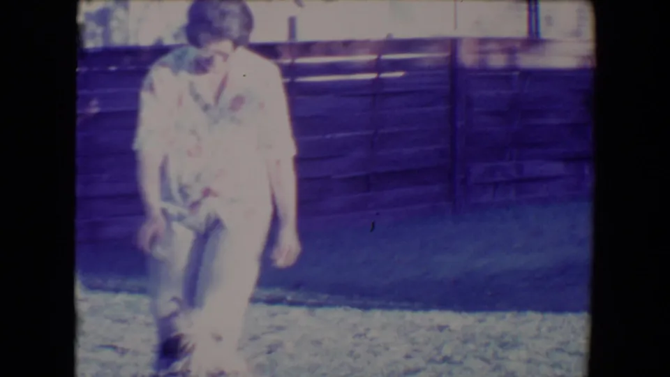 1967 Tucson backyard frame with a woman in a floral shirt and light pants moving beside a small dog on the grass.