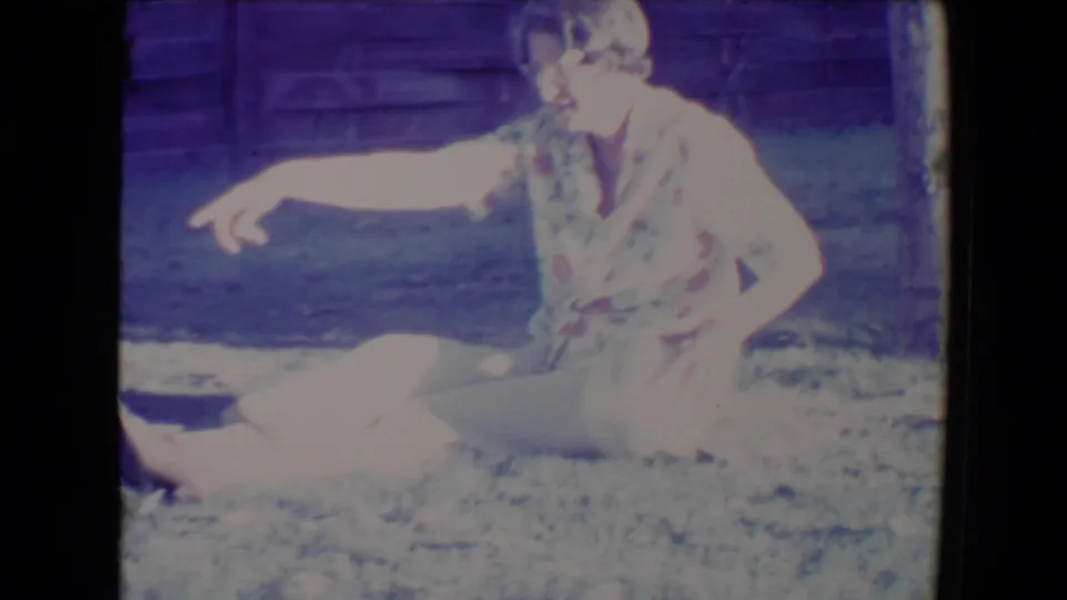 In a 1967 Tucson backyard scene, the woman sits on the grass and points while interacting with the dog nearby.