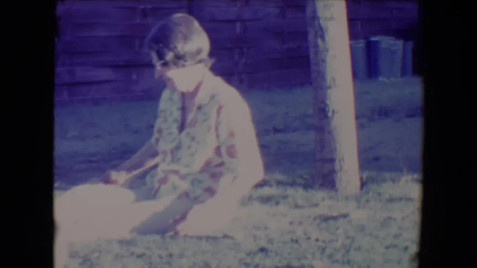 The seated woman appears to reach toward a light-colored dog or object at the edge of the 1967 Tucson backyard frame.
