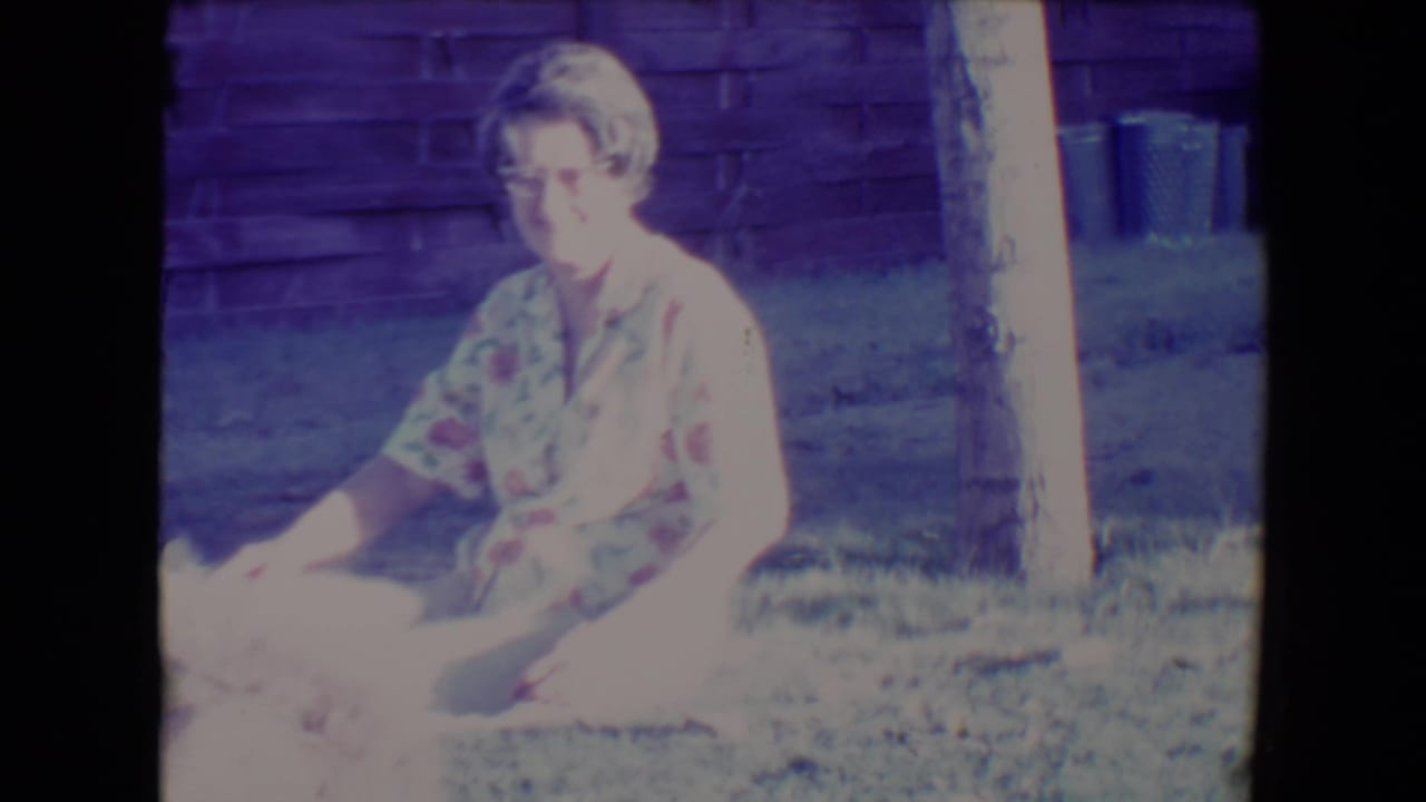 Woman sitting on grass beside a fluffy dog in a sunny backyard.