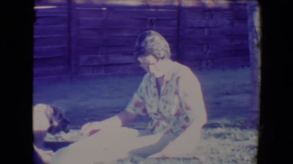 The woman looks down toward the small dog on the lawn, with the wooden backyard fence filling the background.