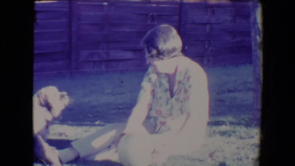 The woman leans forward in the yard as the small dog faces her, captured with strong 8mm color shift and exposure flare.