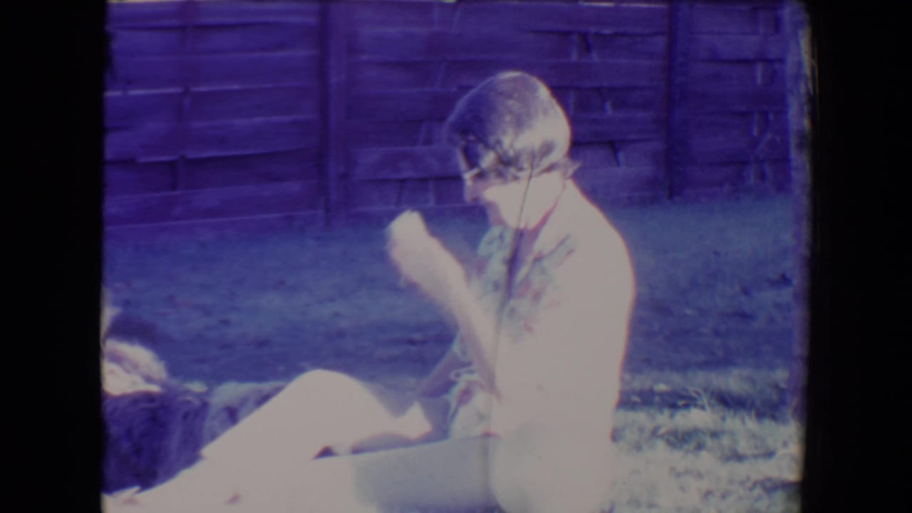 Woman seated on grass beside a shaggy dog in front of a wooden fence.