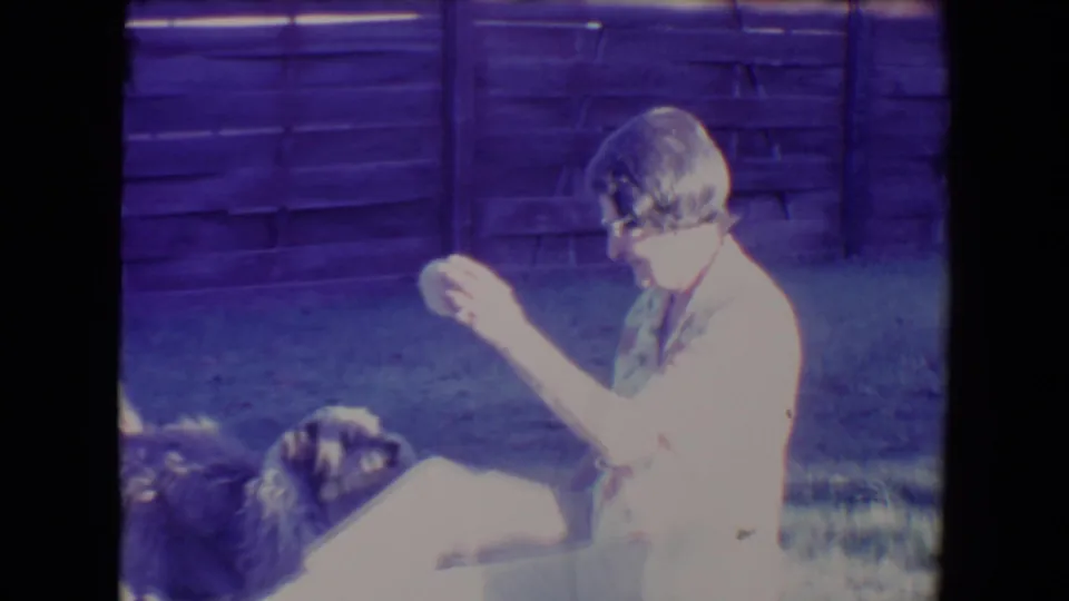 1967 Tucson frame of a woman in bright sun holding a small object while a shaggy dog rests close by on the lawn.