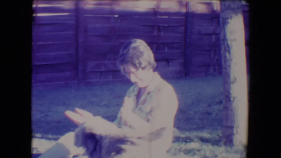1967 Tucson frame showing a woman seated on grass, looking down as the shaggy dog moves partly into the foreground.