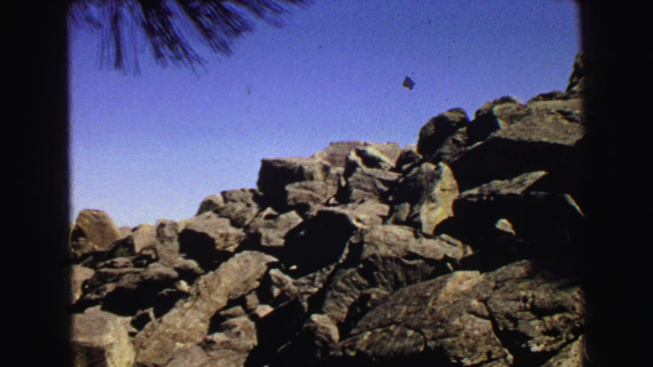 Large boulder pile under blue sky with dark film borders and pine needles at the top.