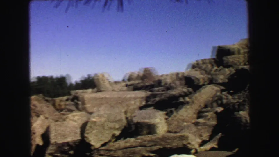 1967 Yellowstone home-movie frame showing a rocky boulder field with distant forest and clear sky, softened by handheld 8mm focus.