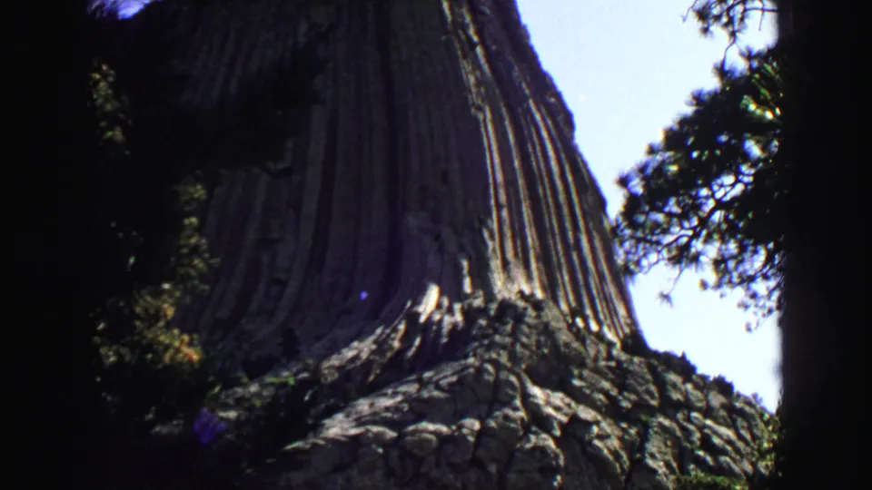 Final 1967 8mm frame holding on Devils Tower's striated rock face with trees at the sides.
