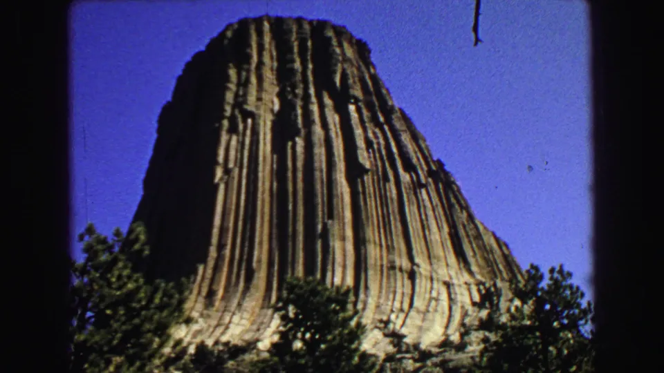 1967 8mm frame with Devils Tower dominating the view, its grooved rock columns rising from trees below.