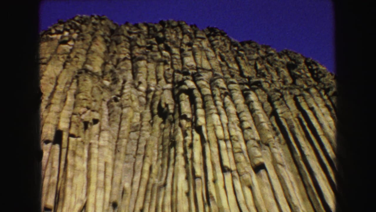 Closer low-angle view of vertical rock columns against blue sky.