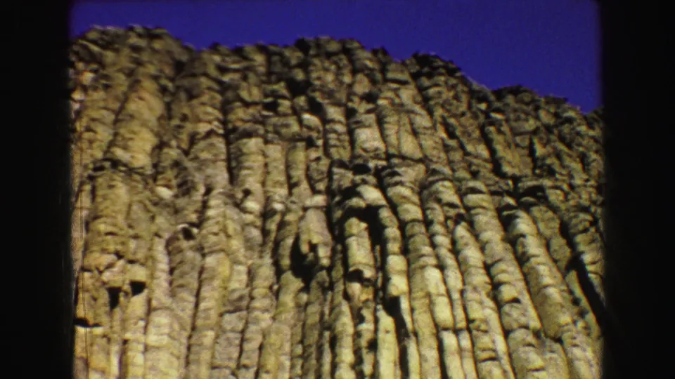 1967 8mm frame with the rock formation filling the view, showing rugged vertical columns and a narrow band of blue sky.