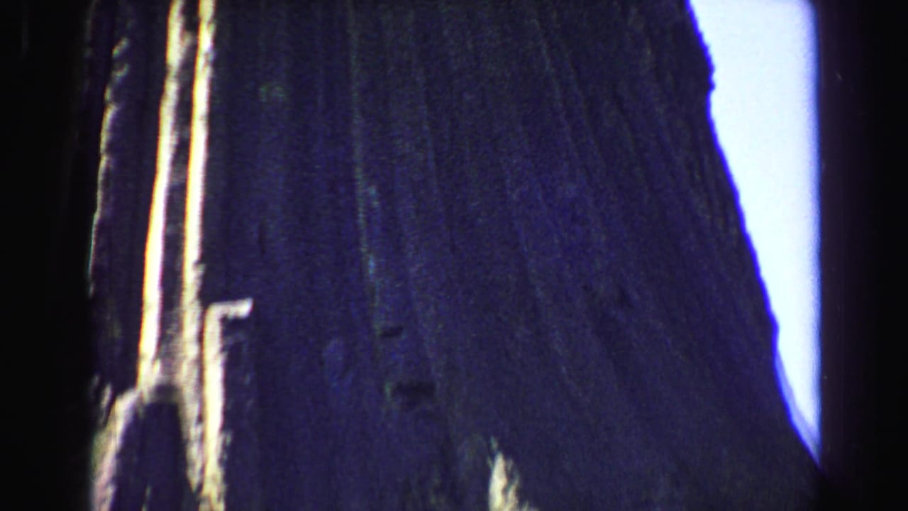 Close upward view of a dark vertical cliff surface with bright sky along the edge.