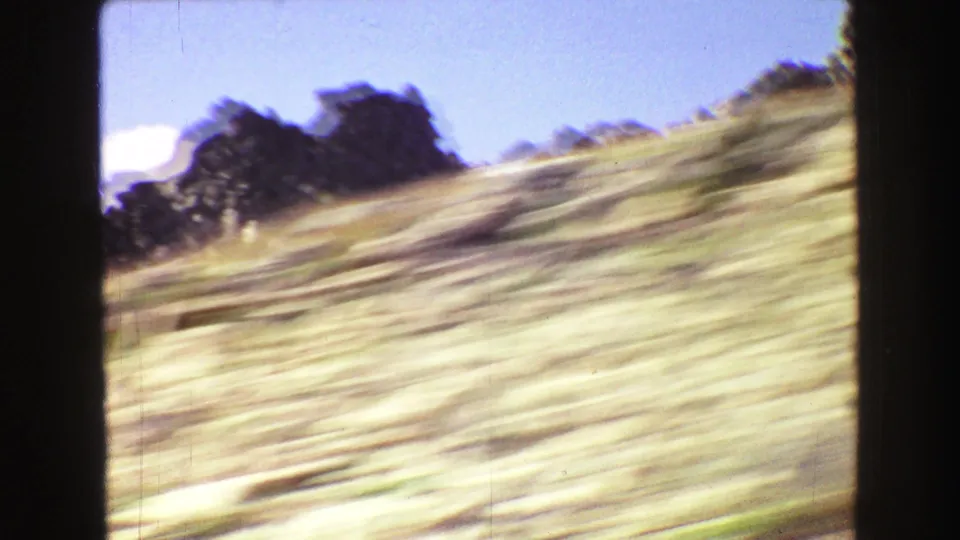 1967 Yellowstone-area 8mm frame showing a blurred dry hillside and dark rocky outcrop under pale blue sky.