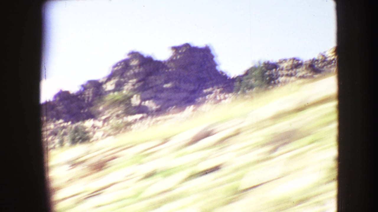 Yellowstone-area road-trip frame with sunlit scrubby slope, dark rocks, and heavy motion blur from a moving car.