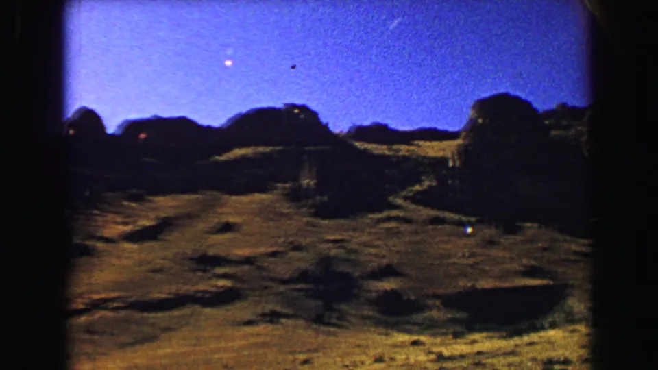 1967 8mm dusk view in the Yellowstone area, with dark ridgelines and low hills silhouetted below a blue-purple sky.