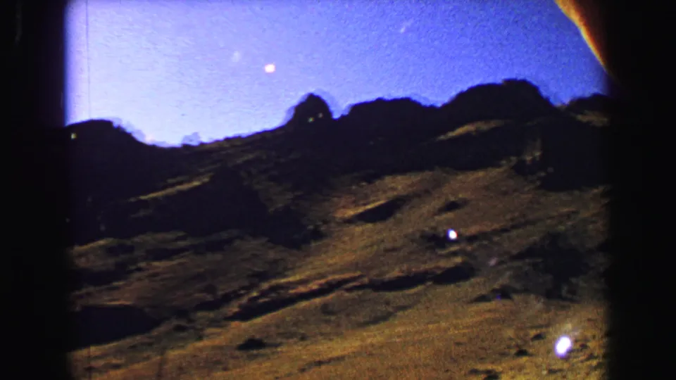 Yellowstone-area 8mm frame at dusk, showing dark mountain forms, uneven ground, and a purple sky with bright film specks.