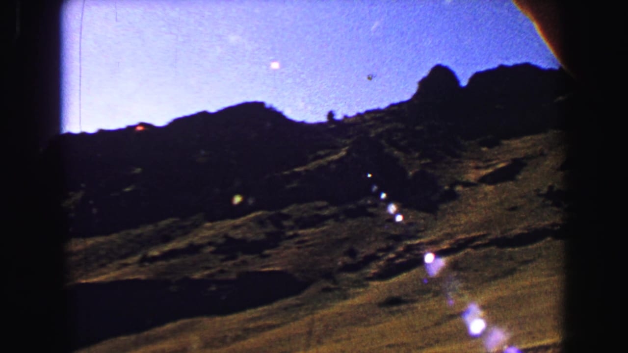 Rugged hills and blue sky seen through a vehicle window with lens flare.