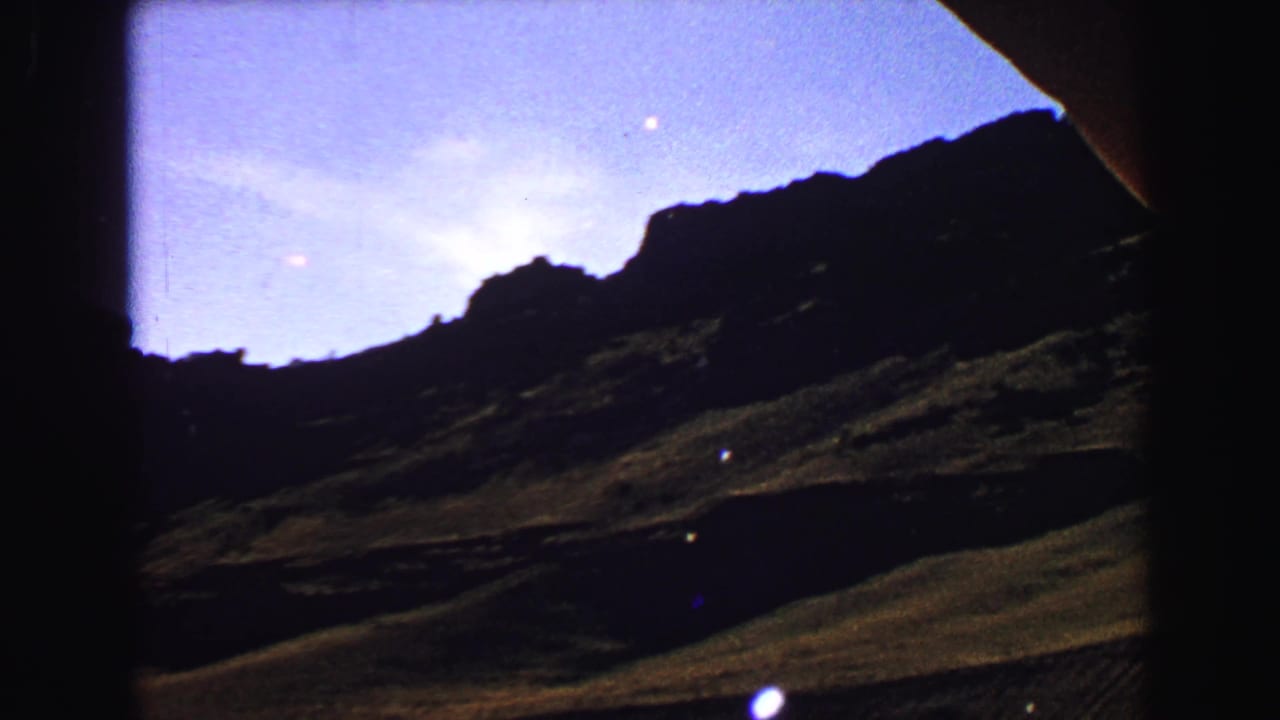 Dark mountain ridge and sloping terrain beneath a bright blue sky.