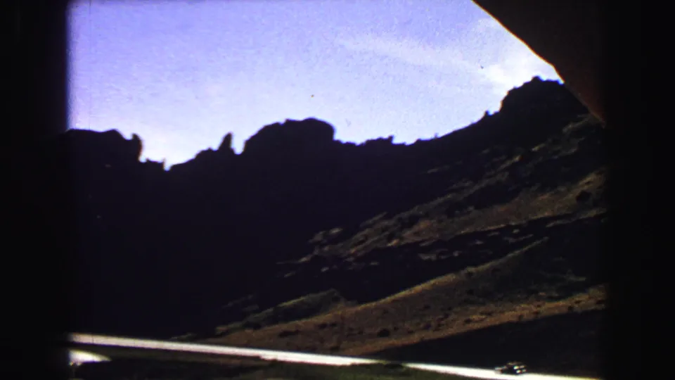 1967 Yellowstone road-view frame showing silhouetted rock formations, sloped ground, road edge, and vehicle-window framing.