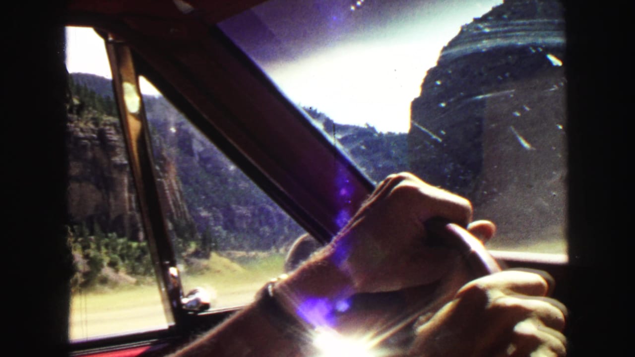 Hands on a steering wheel seen through a car window with canyon cliffs outside.