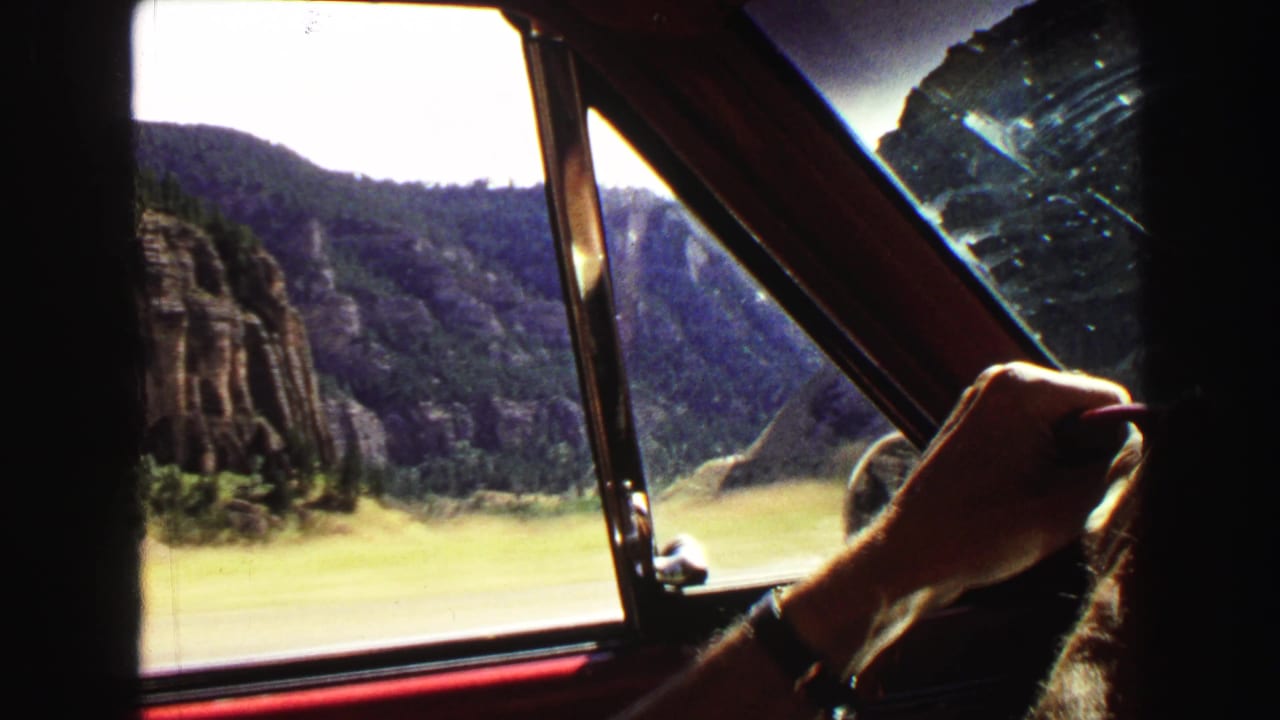Inside-car view in Yellowstone, Wyoming, with a hand near the wheel and canyon scenery visible through the window.