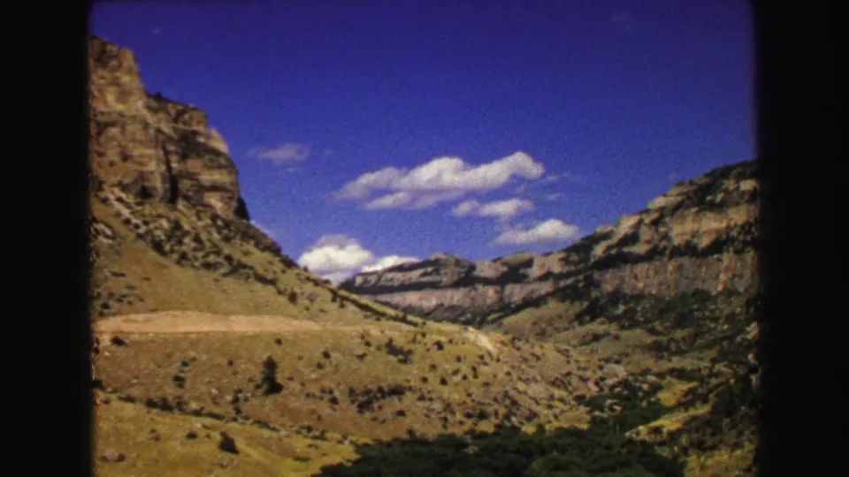Wide 1967 Yellowstone landscape view showing dry grassland, rocky canyon sides, distant ridges, and a bright blue sky.