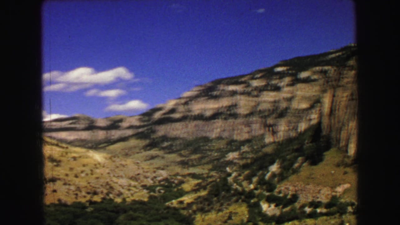 Distant layered cliffs and valley under blue sky with scattered clouds.